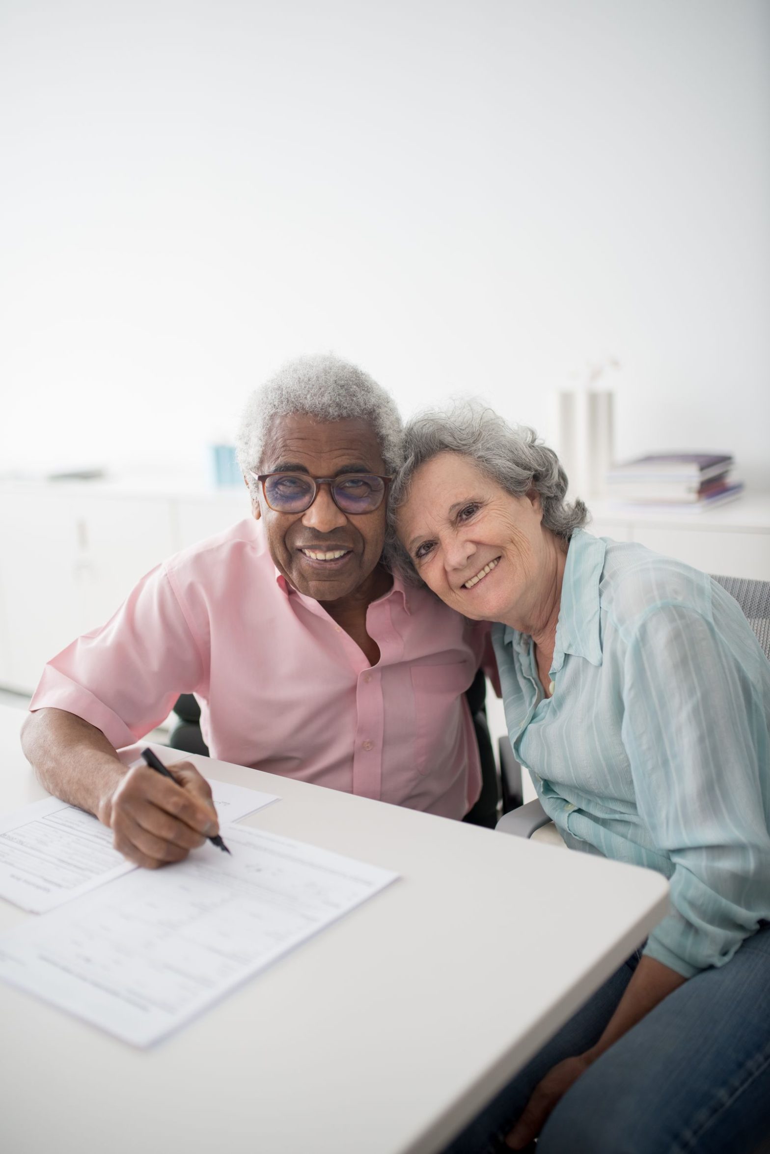 Elderly couple smiling while signing documents at a desk